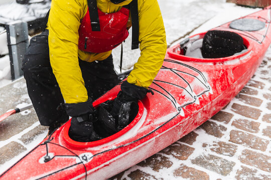 Adventurer Preparing Red Kayak on Snowy Cobblestone Harbor