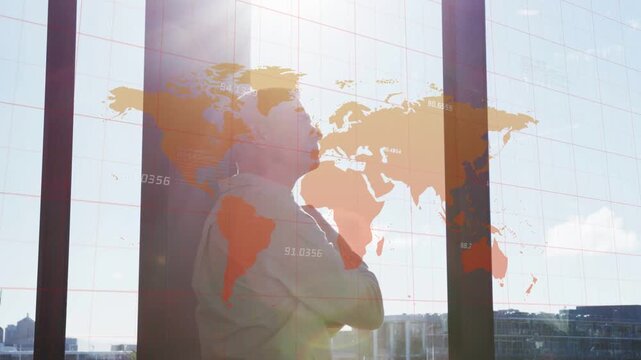 Man standing by glass window at office, wearing button-up shirt, studying orange world map overlay