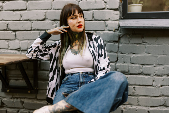 Woman Sitting Casually Against a Gray Brick Wall in a City