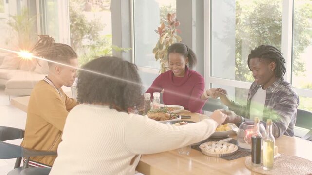 Four adults holding hands bowing heads, thanking while serving meal, sunlight flaring for marketing