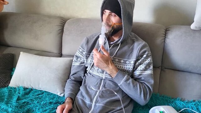Caucasian man treating throat and bronchi with a portable nebulizer, effective flu therapy, home wellness lifestyle, medical treatment.