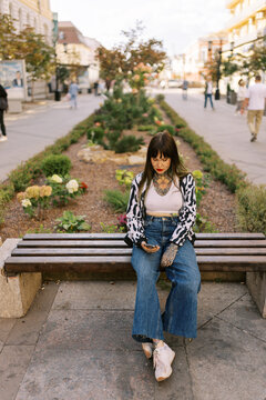 Woman Sitting on Bench in City Park With Flowers in Background