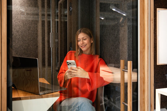 Woman relaxing in soundproof booth with laptop and phone