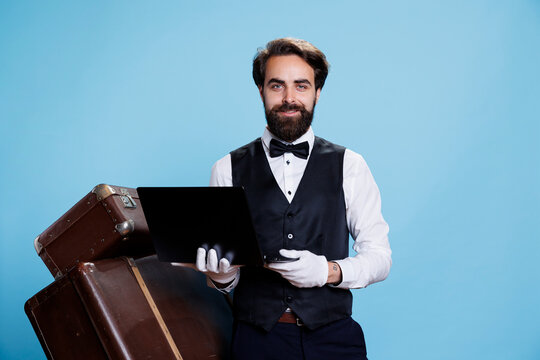 Bellman holds laptop in hand to show professionalism of hospitality industry, showcases proficiency in utilizing technology to provide services. Porter with gloves making online bookings.