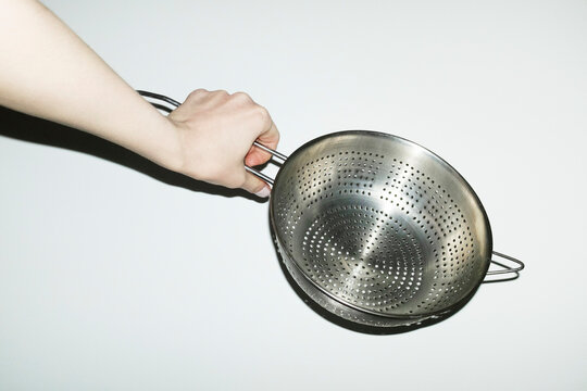 Hand holding shiny silver kitchen tool strainer with flashlight