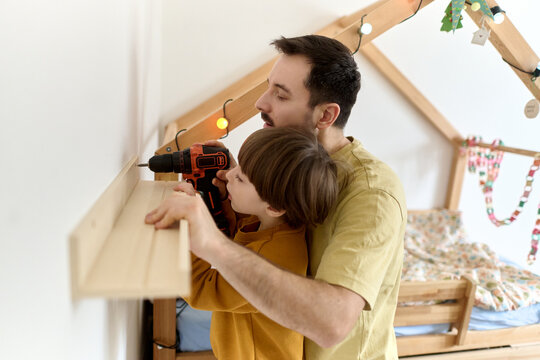 Father guiding son using drill to mount shelf