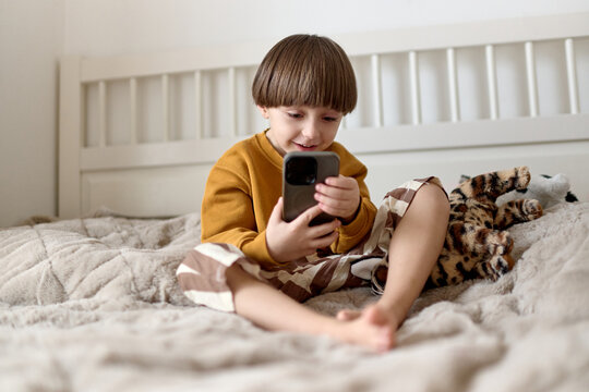 Smiling boy using smartphone while sitting on bed