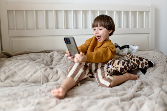 Child taking selfie with smartphone on bed
