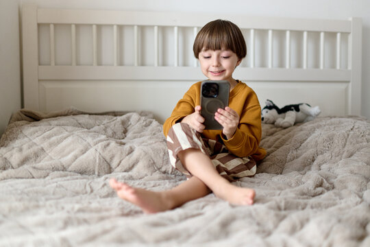 Smiling boy using smartphone while sitting on bed