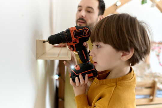 Little boy using drill to install wooden shelf