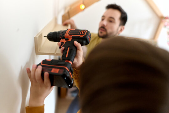 Child Holding Drill While Father Mounts Shelf