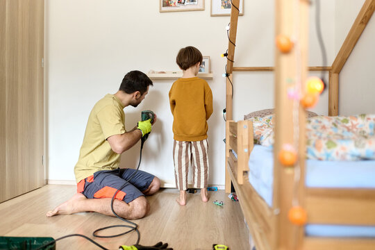 Father Installing Shelf While Son Measures in Bedroom
