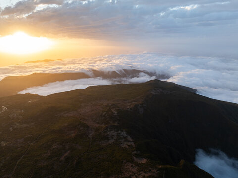 Aerial view of the Bica da Cana viewpoint overlooking a thick sea of clouds and rugged mountain peaks during a golden sunset in Ponta do Sol, Madeira, Portugal.