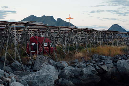 Red camper van under traditional fish drying racks in Lofoten