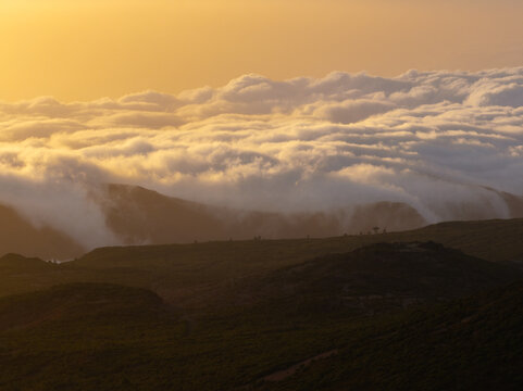 Aerial view of the Bica da Cana mountain ridge with thick clouds rolling over the peaks during a golden sunset in Ponta do Sol, Madeira, Portugal.