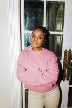 Woman with braided hair and pink sweater standing at home ugc