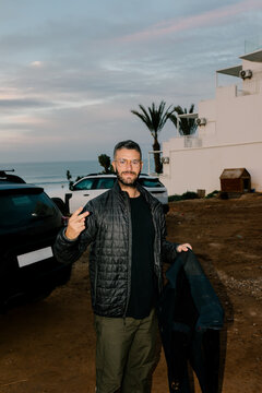 Surfer waving at the camera while holding his wetsuit
