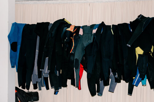 Several surfing wetsuits hanging from a clothesline indoors