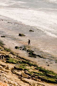 Surfer coming out of the sea on the rocky coast of a beach in Morocco