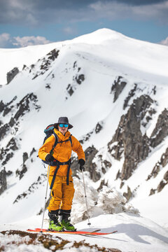 Man in an orange jacket putting on skis,  and preparing  to ride 