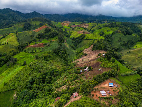 Aerial view of Yun Lai Viewpoint featuring lush green mountain slopes, agricultural patches, and small rural houses under a misty sky in Wiang Tai, Mae Hong Son, Thailand.