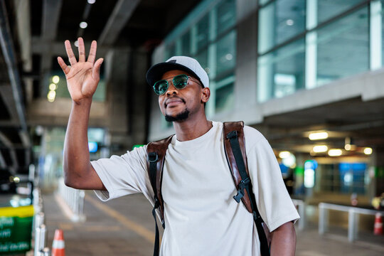 Man with backpack waves in airport or parking garage.