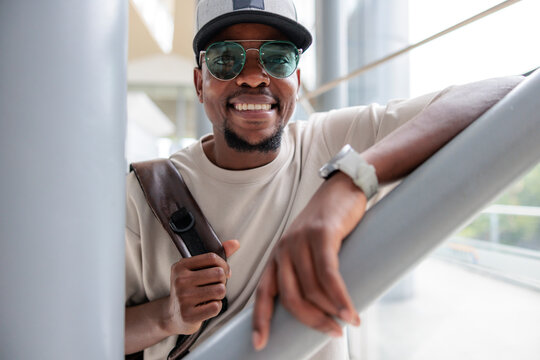 Smiling man with sunglasses and backpack leans on railing.