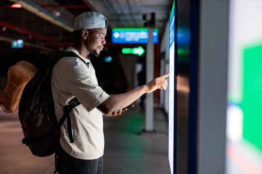 Man uses touch screen kiosk in public transit area.