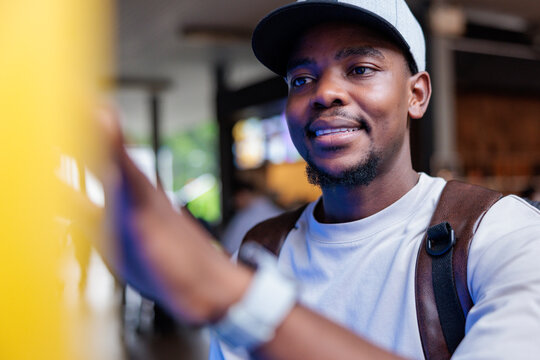 Smiling man in cap with backpack uses a self-service kiosk