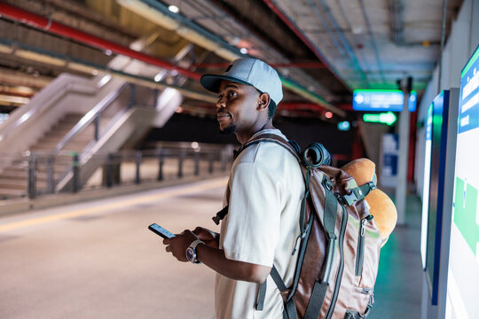 Man with backpack checks phone at train station.
