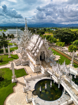 Aerial view of the intricate white architecture of Wat Rong Khun temple with its ornate spires and bridge over a pond in Pa O Don Chai, Chiang Rai, Thailand.