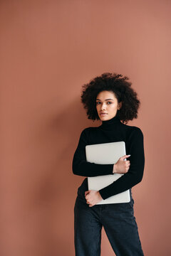 Confident Woman Poses With Laptop Against Warm Backdrop