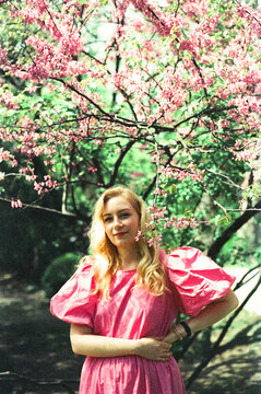 Young Woman Stands Under Cherry Blossom Tree in Springtime Garden