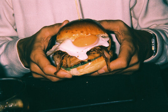 a man holds a burger with a fried egg and cheese, 35mm film
