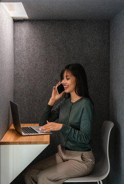 Woman multitasking with phone and laptop in modern booth
