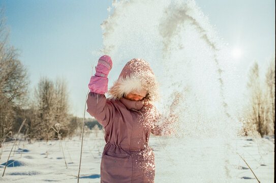 Child Throwing Snow in Sunny Winter Landscape