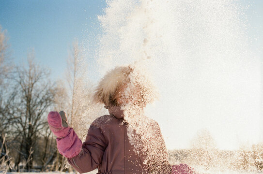 Child Tossing Snow in Bright Winter Landscape