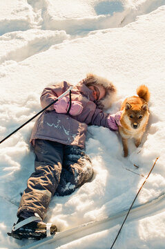 Child Resting in Snow with Shiba Inu After Skiing