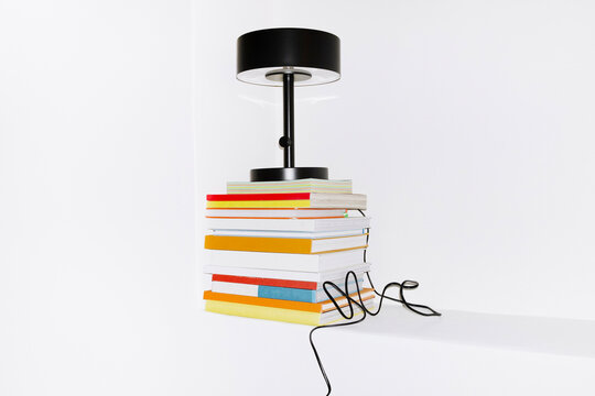 Pile of colourful paper books and black minimal lamp with wire