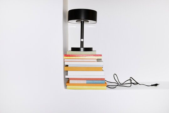 Pile of colourful paper books and black minimal lamp with wire