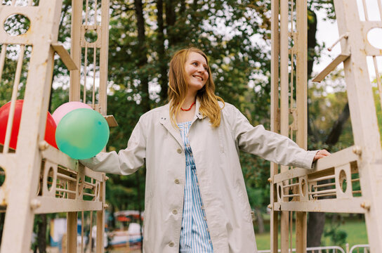 Young Woman Stands on Playground Structure With Colorful Balloons