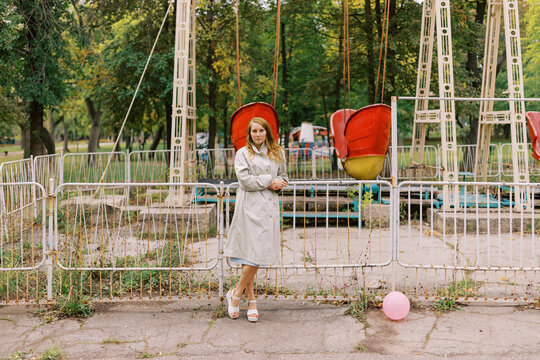Woman Stands by Fenced Amusement Park Rides on a Sunny Day