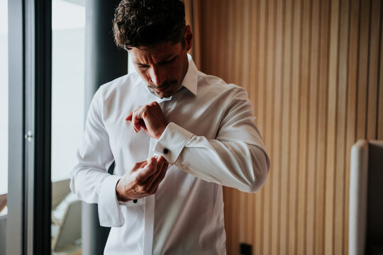 Handsome man fastening cufflinks in natural window light