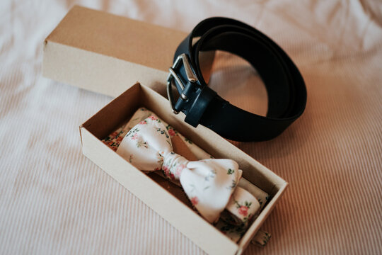 Floral bow tie and leather belt laid out before wedding