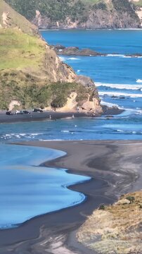 People enjoy a sunny day at Marokopa, Waikato, New Zealand. The black sand beach and rugged coastline offer a picturesque setting for recreation and relaxation.
