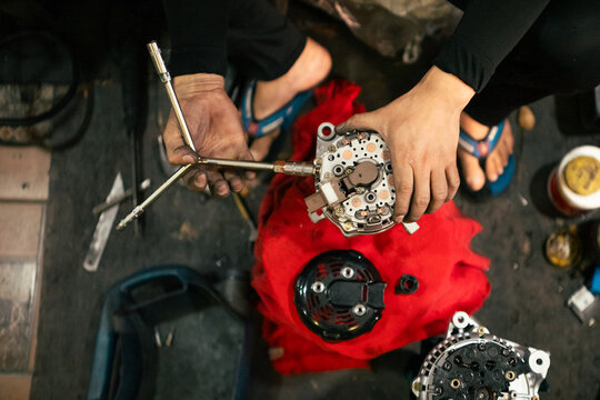 Mechanic inspecting and repairing vehicle alternator using a wrench