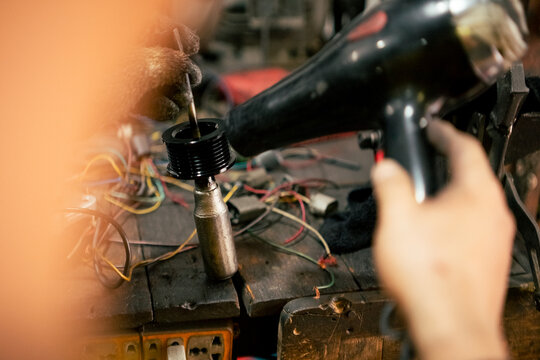 Mechanic repairing engine part using tools and hairdryer in workshop
