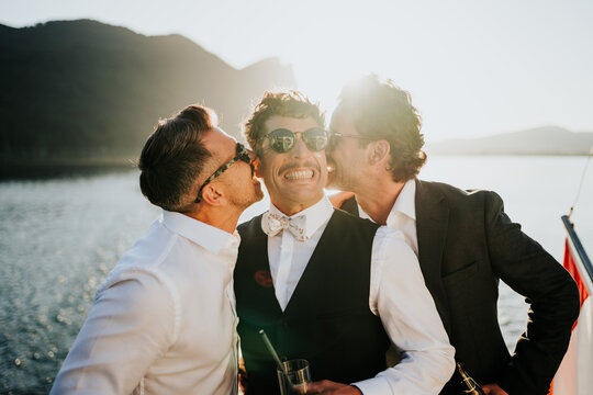 Playful friends kissing groom during joyful celebration on a boa