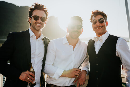 Stylish groom and friends enjoying drinks during lakeside celebr