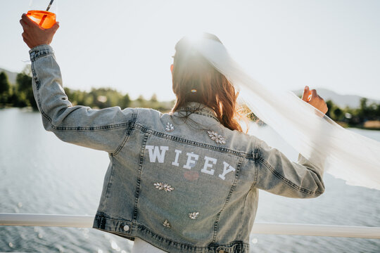 Bride raising cocktail with flowing veil during sunset wedding c